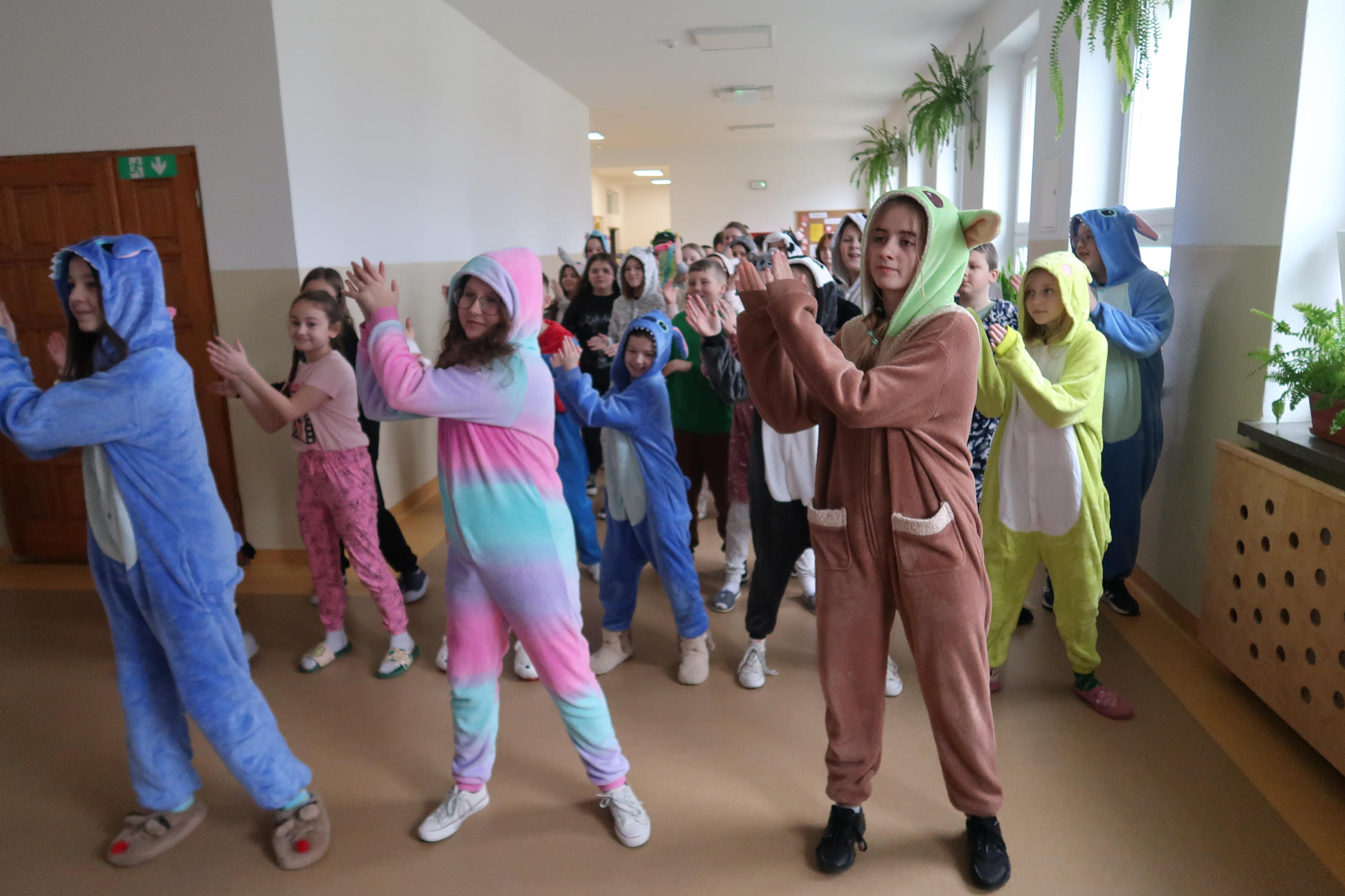 Młodzież szkolna przebrana w kolorowe piżamy zgromadzona na korytarzu szkolnym wykonuje układ taneczny