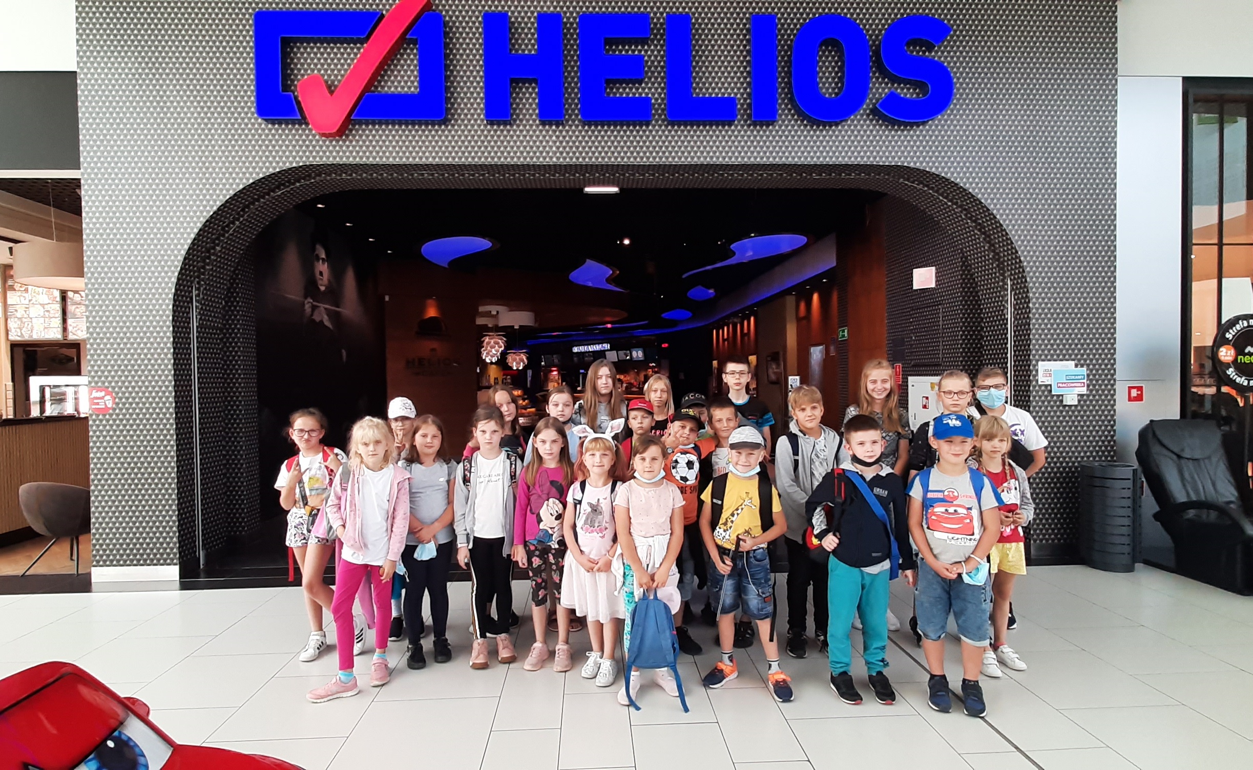 Zdjęcie przedstawiające grupę dzieci uczestniczących w półkoloniach letnich przed wejściem do Kina Helios w Starachowicach