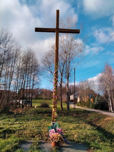 Krzyż drewniany usytuowany przy drodze powiatowej Nr 0734T i drodze wewnętrznej po lewej stronie w kierunku Mierzanowic