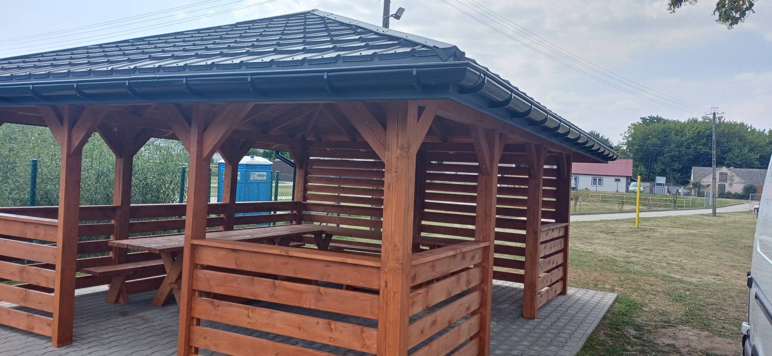 Drewniana brązowa altana z blaszanym dachem i rynnami w kolorze czarnym