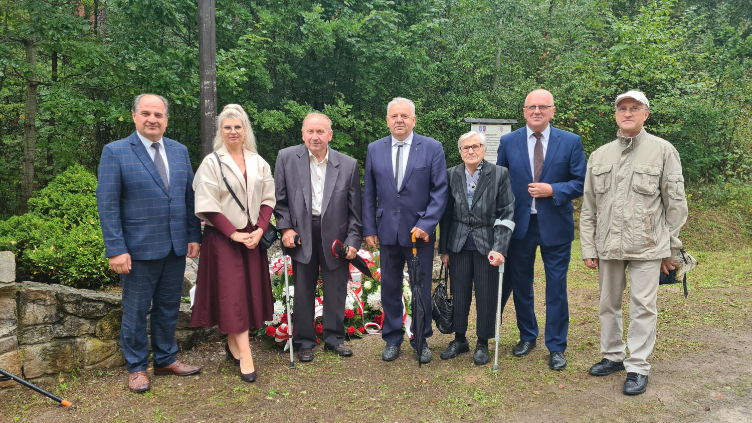 Uczczono pamięć o mieszkańcach dawnych Orłowin Zdjęcie grupowe w miejscu pamięci, w tle wiązanki i las