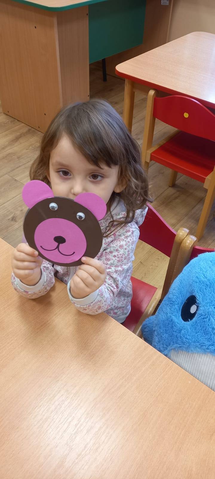 Uczennica prezentująca kolorową głowę misia zrobionego z papieru